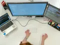 Postazione di lavoro con laptop e due monitor che mostrano codice. Una persona digita, concentrata sul suo lavoro con python, per continuare a sviluppare.