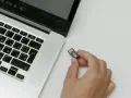 Una mano tiene una chiavetta USB con un simbolo di chiave, pronta per essere inserita in un laptop. Chissà quanto è un terabyte di dati da archiviare!