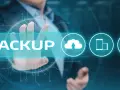 Un uomo tocca la parola "BACKUP" su uno schermo futuristico, con icone di cloud, smartphone e laptop.