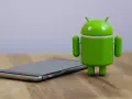 Un cellulare che si impalla, con l'iconico robot verde Android accanto, su un tavolo di legno.