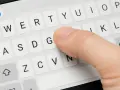 Dito come ingrandire la tastiera del cellulare: un dito preme il tasto "G" su una tastiera virtuale.