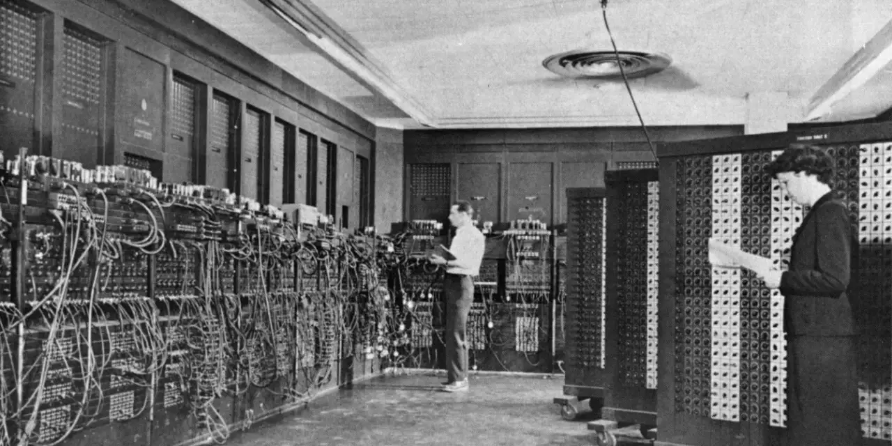 Il computer ENIAC, un gigante di cavi e pannelli, con due persone che lavorano al suo interno.