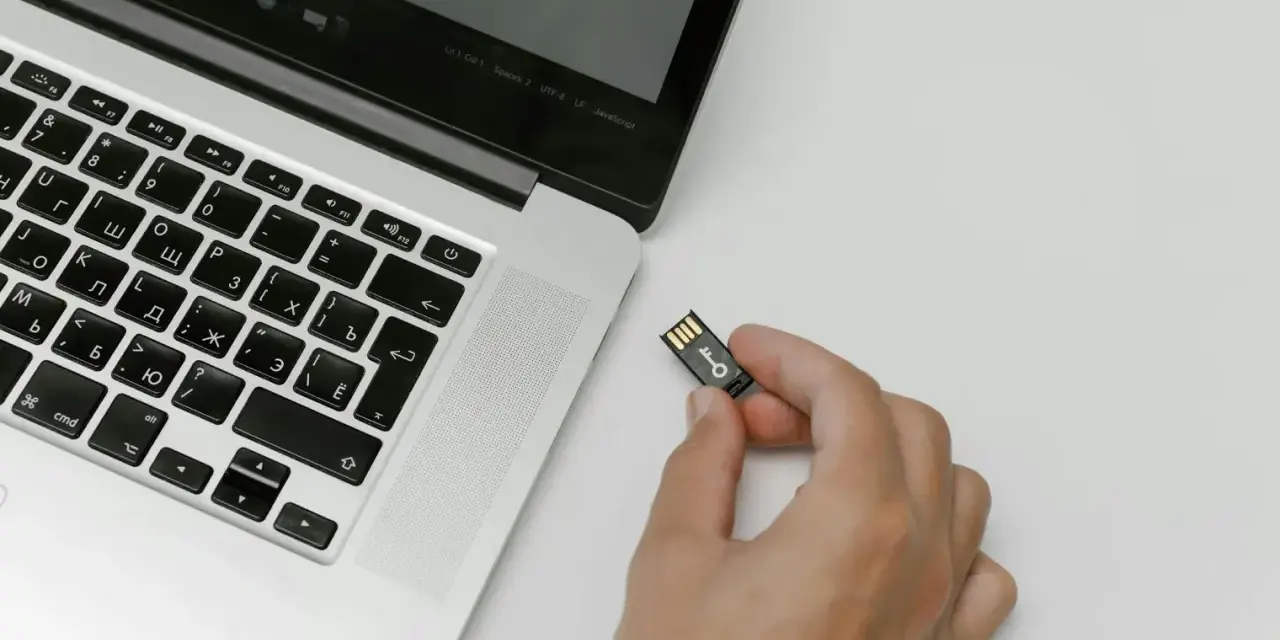 Una mano tiene una chiavetta USB con un simbolo di chiave, pronta per essere inserita in un laptop. Chissà quanto è un terabyte di dati da archiviare!