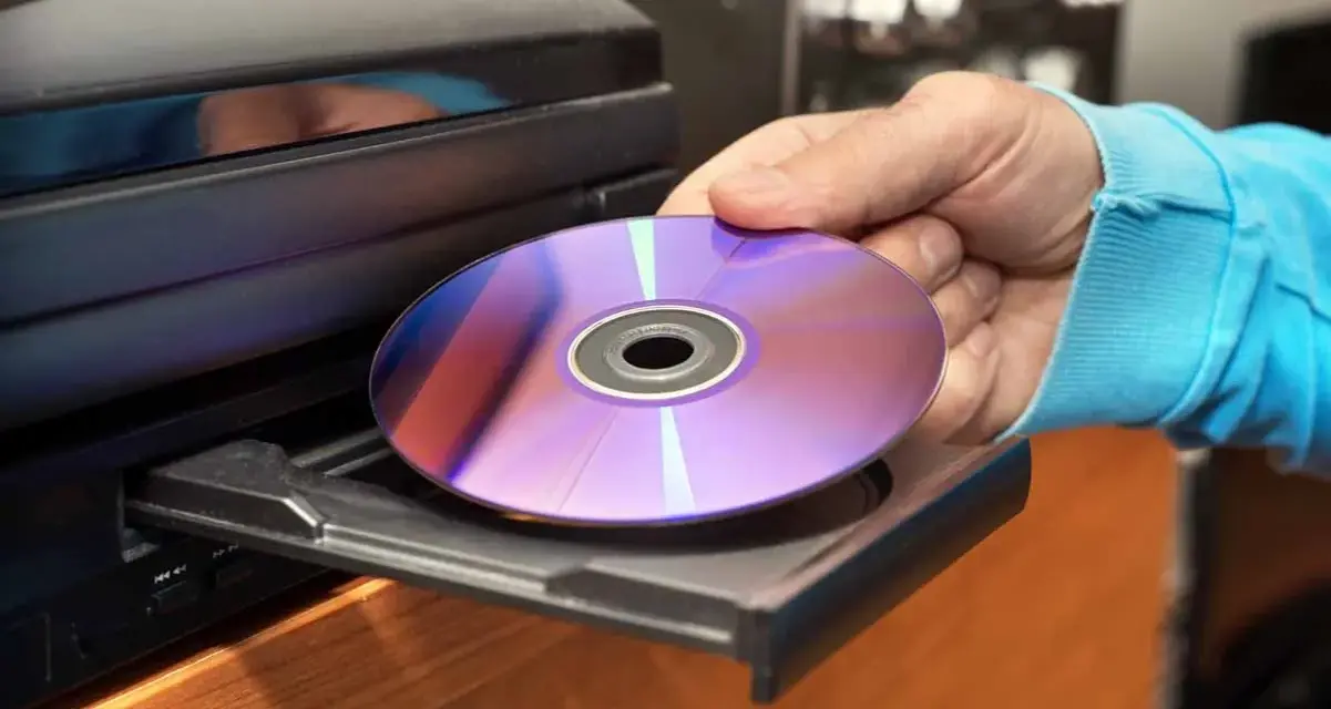 Mano inserisce un CD-ROM nel lettore. Il CD-ROM, con riflessi viola e blu, è pronto per essere letto, mostrando il suo significato di supporto di memoria.