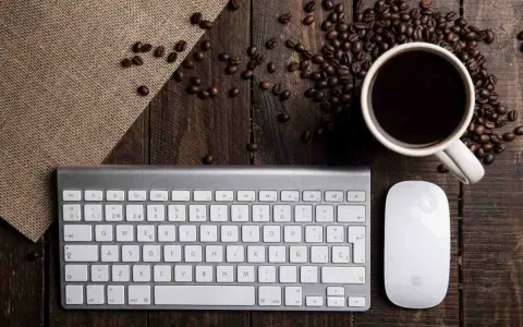 Tastiera PC con tasti funzione, mouse e tazzina di caffè su un tavolo di legno rustico, circondata da chicchi di caffè.