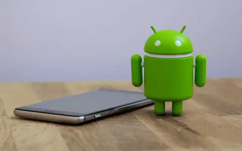 Un cellulare che si impalla, con l'iconico robot verde Android accanto, su un tavolo di legno.