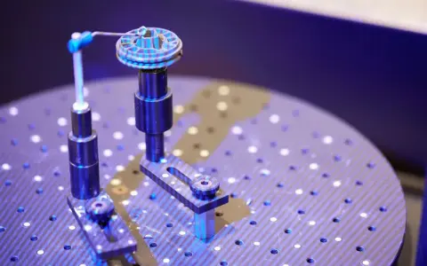 Un oggetto circolare con scanalature è fissato su un supporto. Un braccio metallico con una punta blu si avvicina per analizzarlo. Questo è un esempio di come funziona uno scanner 3D.