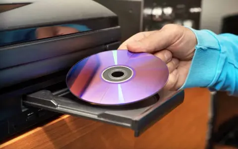 Mano inserisce un CD-ROM nel lettore. Il CD-ROM, con riflessi viola e blu, è pronto per essere letto, mostrando il suo significato di supporto di memoria.