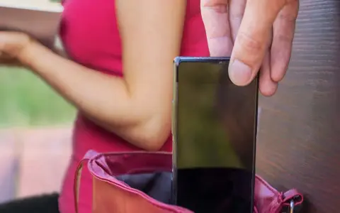 Mano che ruba un telefono da una borsa. Bloccare telefono rubato con IMEI è la soluzione.