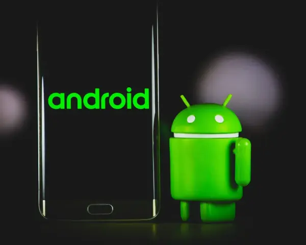Un robot Android verde accanto a uno smartphone con il logo Android. La sincronizzazione automatica Android è fondamentale per mantenere i dati aggiornati.