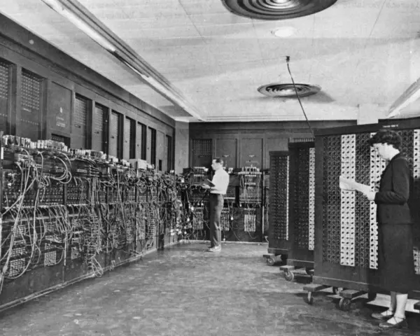 Il computer ENIAC, un gigante di cavi e pannelli, con due persone che lavorano al suo interno.