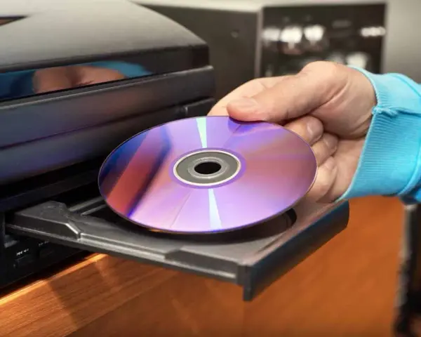 Mano inserisce un CD-ROM nel lettore. Il CD-ROM, con riflessi viola e blu, è pronto per essere letto, mostrando il suo significato di supporto di memoria.