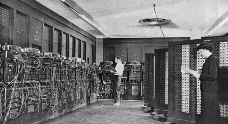 Il computer ENIAC, un gigante di cavi e pannelli, con due persone che lavorano al suo interno.