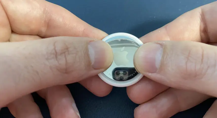 Mani che premono per sostituire la batteria di un AirTag.