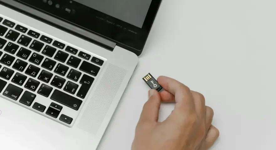 Una mano tiene una chiavetta USB con un simbolo di chiave, pronta per essere inserita in un laptop. Chissà quanto è un terabyte di dati da archiviare!
