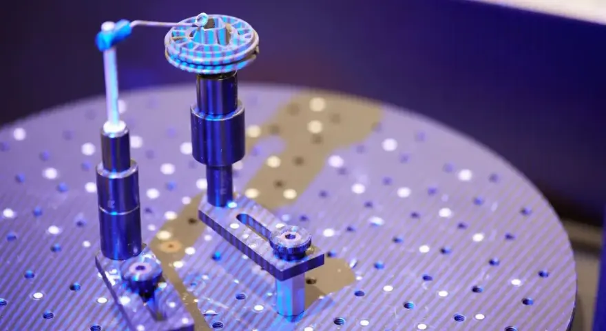 Un oggetto circolare con scanalature è fissato su un supporto. Un braccio metallico con una punta blu si avvicina per analizzarlo. Questo è un esempio di come funziona uno scanner 3D.