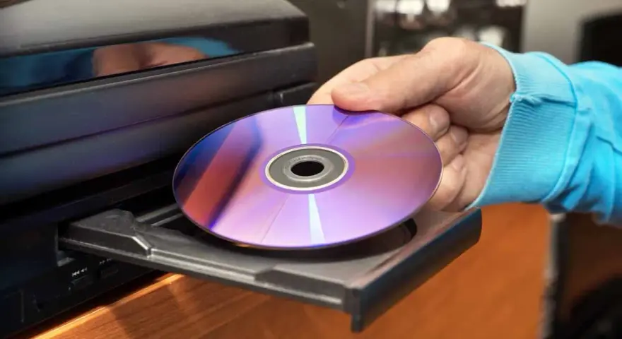 Mano inserisce un CD-ROM nel lettore. Il CD-ROM, con riflessi viola e blu, è pronto per essere letto, mostrando il suo significato di supporto di memoria.