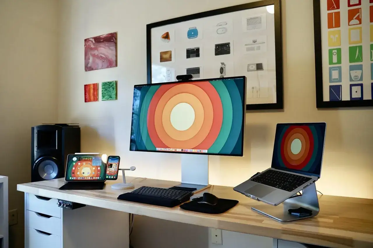 Postazione di lavoro con un grande monitor, un laptop e un iPad, tutti con sfondi colorati. Si vede cos'è il Mac, un ecosistema tecnologico.