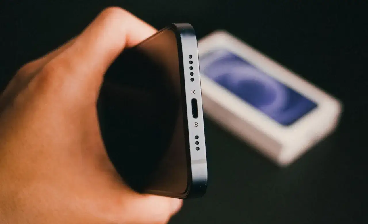 Mano che tiene uno smartphone, pronto a bloccare telefono rubato con imei. Sullo sfondo, la scatola del dispositivo.