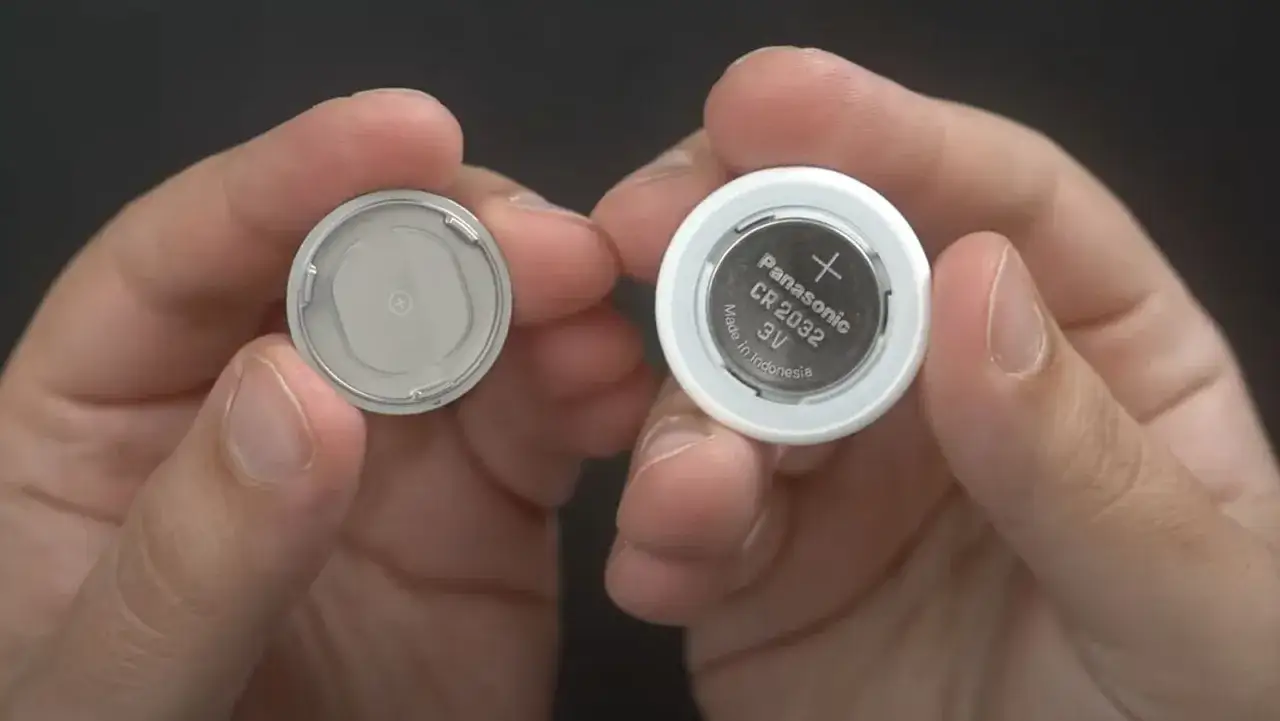 Mani che mostrano una batteria CR2032 Panasonic, la batteria per AirTag, e il suo alloggiamento.