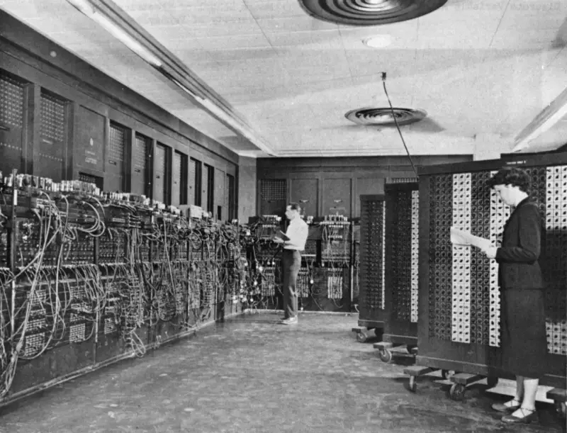 Il computer ENIAC, un gigante di cavi e pannelli, con due persone che lavorano al suo interno.